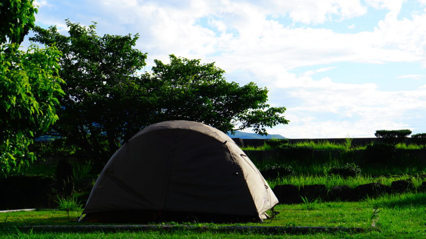 青空の下、木々に囲まれた芝生の区画サイトに設営されたソロキャンプ用のテント。長崎県川原大池公園キャンプ場の様子。